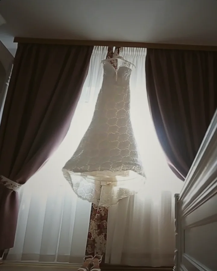 Vestido de novia colgado frente a una ventana con cortinas, antes de la boda