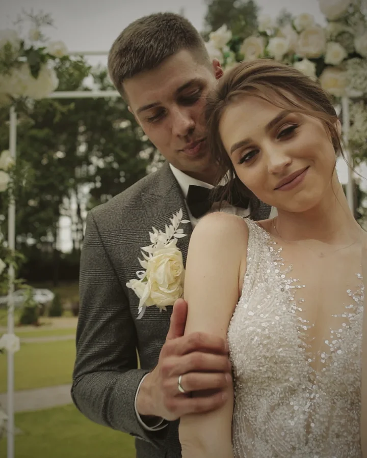 Novios abrazados bajo un arco de flores blancas el día de su boda