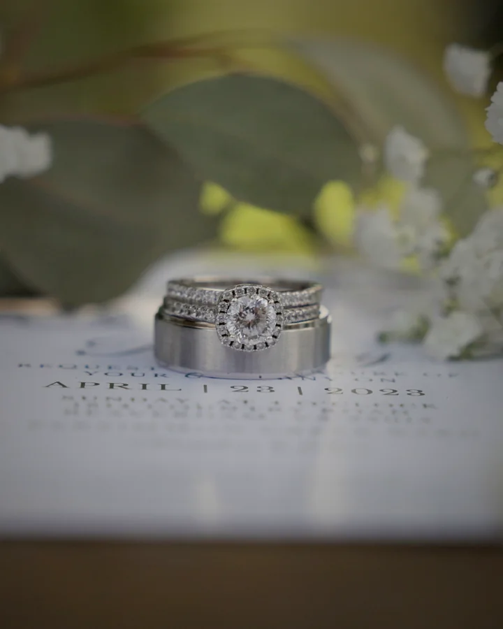 Argollas de matrimonio sobre la invitación de boda, entre flores blancas