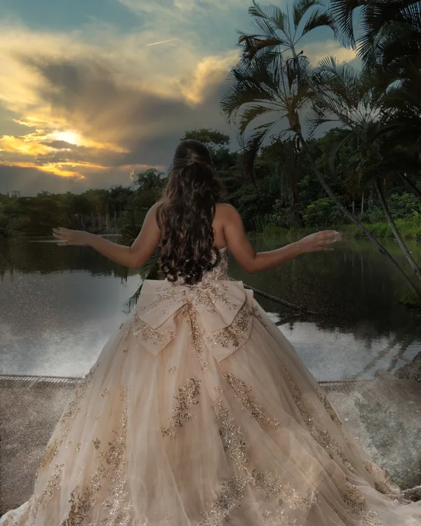 Quinceañera de espaldas con los brazos abiertos frente a un lago al atardecer