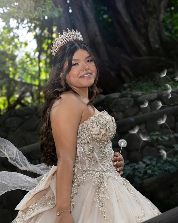 Quinceañera sosteniendo un diente de león, con el velo flotando en el aire