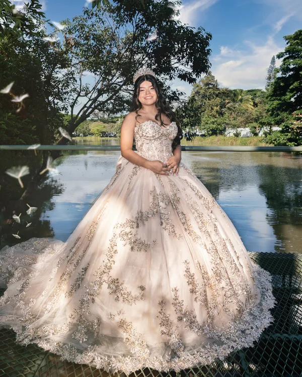 Quinceañera con el vestido completo extendido junto a un lago, bajo un cielo azul
