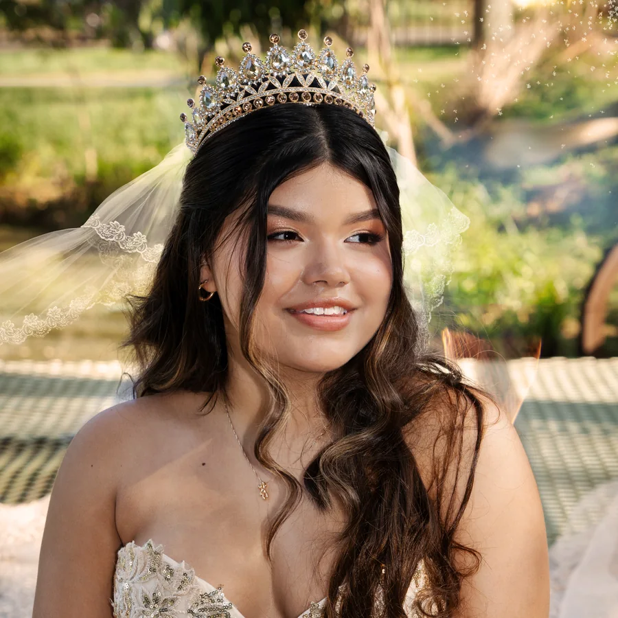 Quinceañera sonriente con tiara y velo, con vestido champaña bordado en dorado