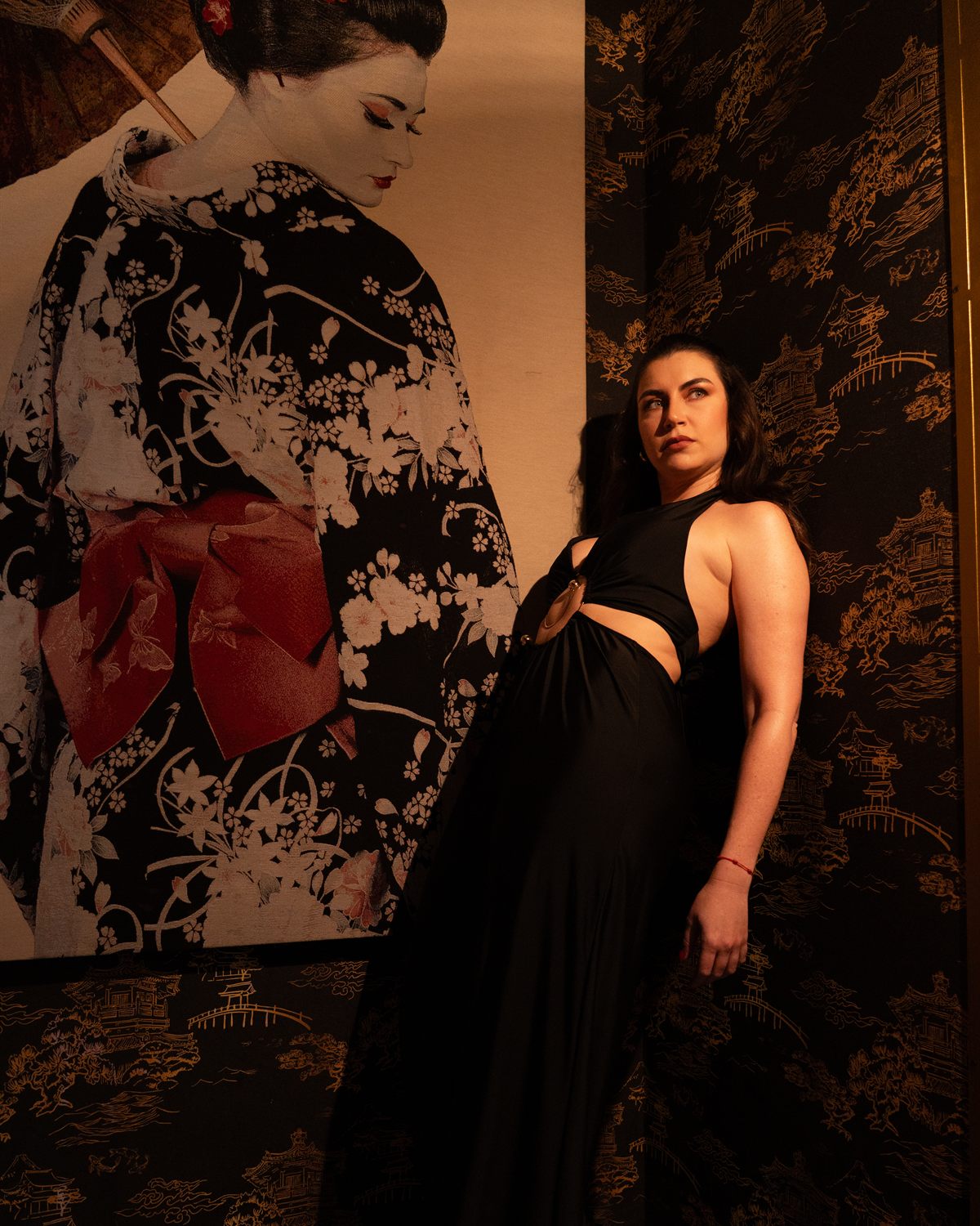 Modelo con vestido negro junto al mural de la geisha, con luz cálida lateral