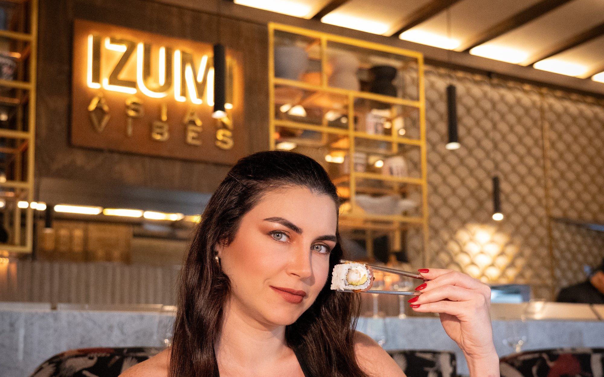 Modelo sosteniendo una pieza de sushi con los palillos, bajo el letrero luminoso IZUMI