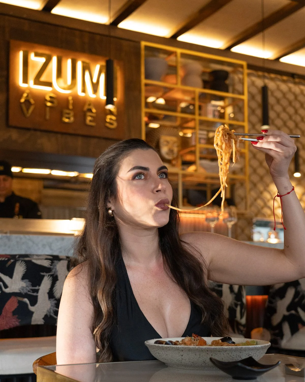 Modelo levantando fideos con los palillos bajo el letrero luminoso IZUMI