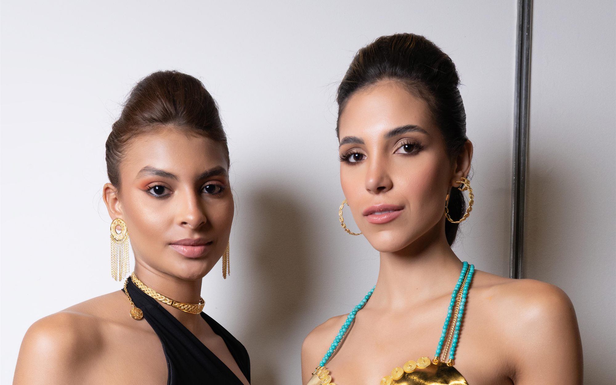 Dos modelos con piezas de joyería dorada sobre fondo claro de estudio